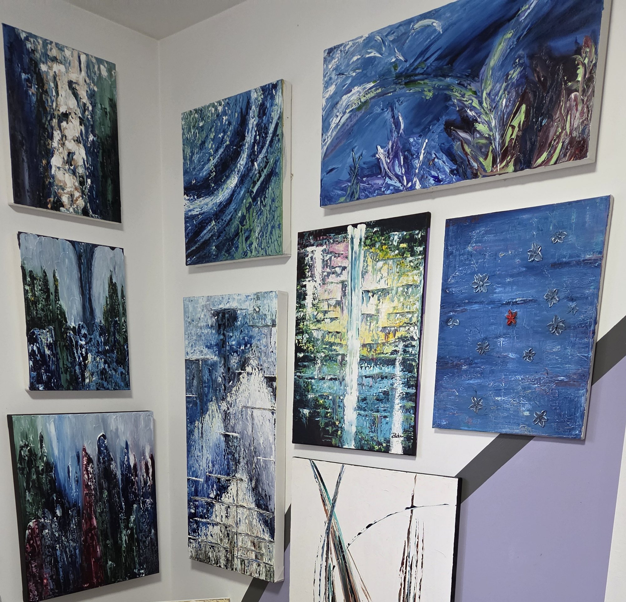 Mur de l'atelier de Rouleau couvert de toiles abstraites aux tons bleus, verts et blancs